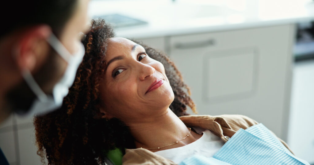 A woman sits in a dental chair while dentist talks about appointment